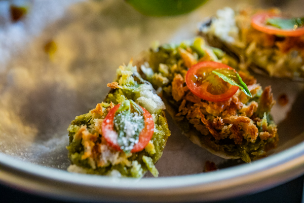 Pesto Rockefeller Oysters: oysters topped with fresh basil, toasted pine nuts, parmesan, cherry tomatoes, and crispy panko, served over rock salt.